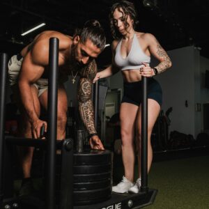 Fit male adding a weight on to an exercise sled while a woman stands behind him