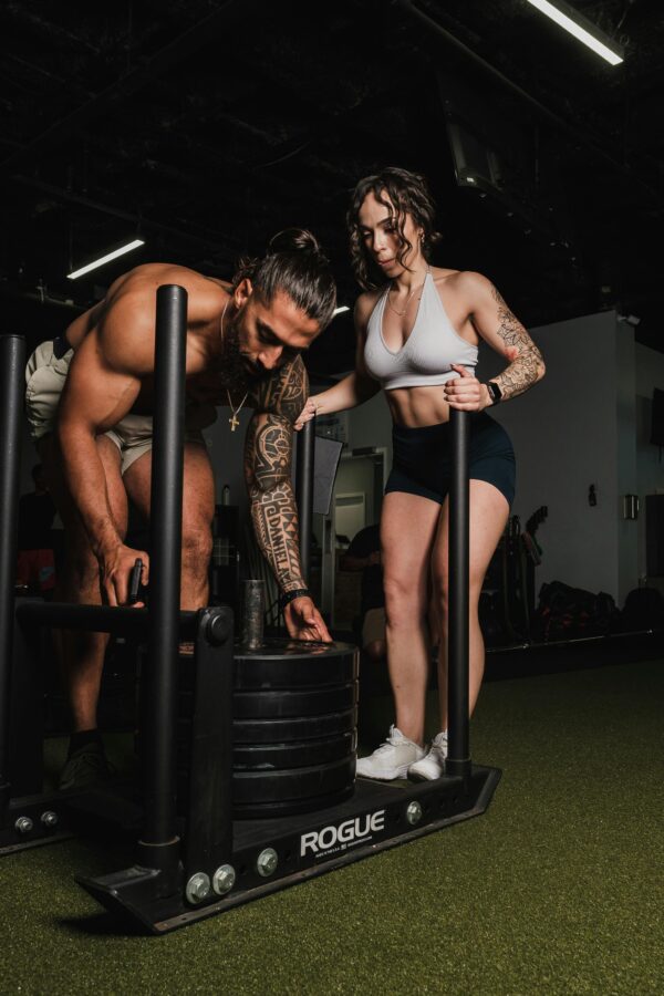 Fit male adding a weight on to an exercise sled while a woman stands behind him